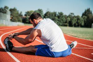 Man sitting on a running track, stretching his calves and hamstrings before a run.